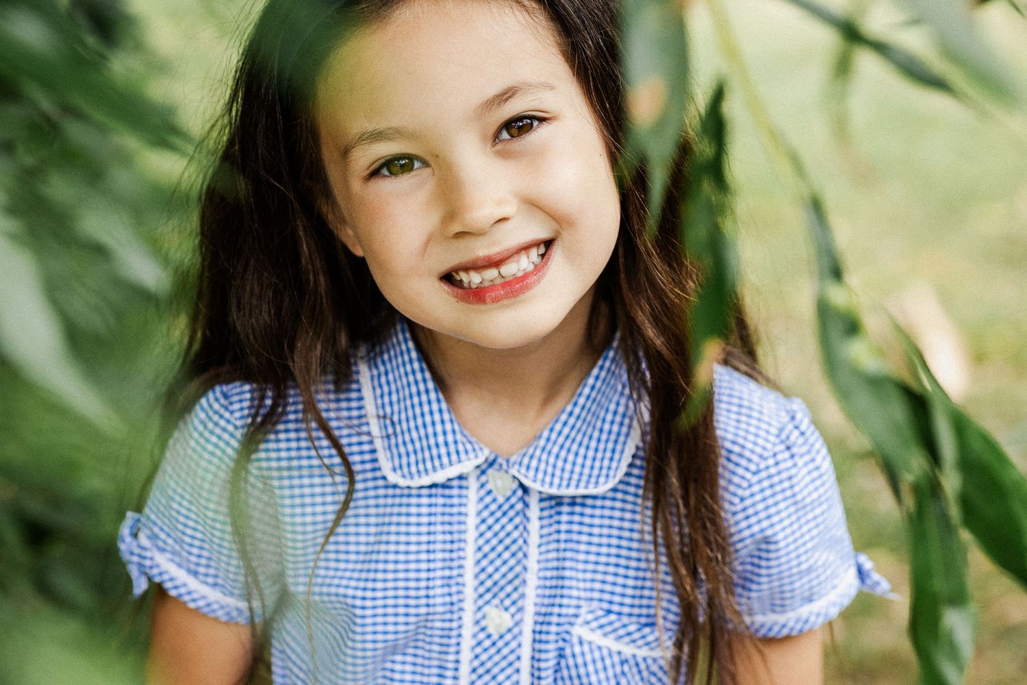 A school child smiles to camera. She looks relaxed and at natural as she stands under a willow tree. Outdoor Bristol school photos.