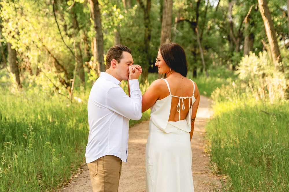 Romantic outdoor photo shoot in a sunlit forest path showing tender moments between loving couple in white attire.