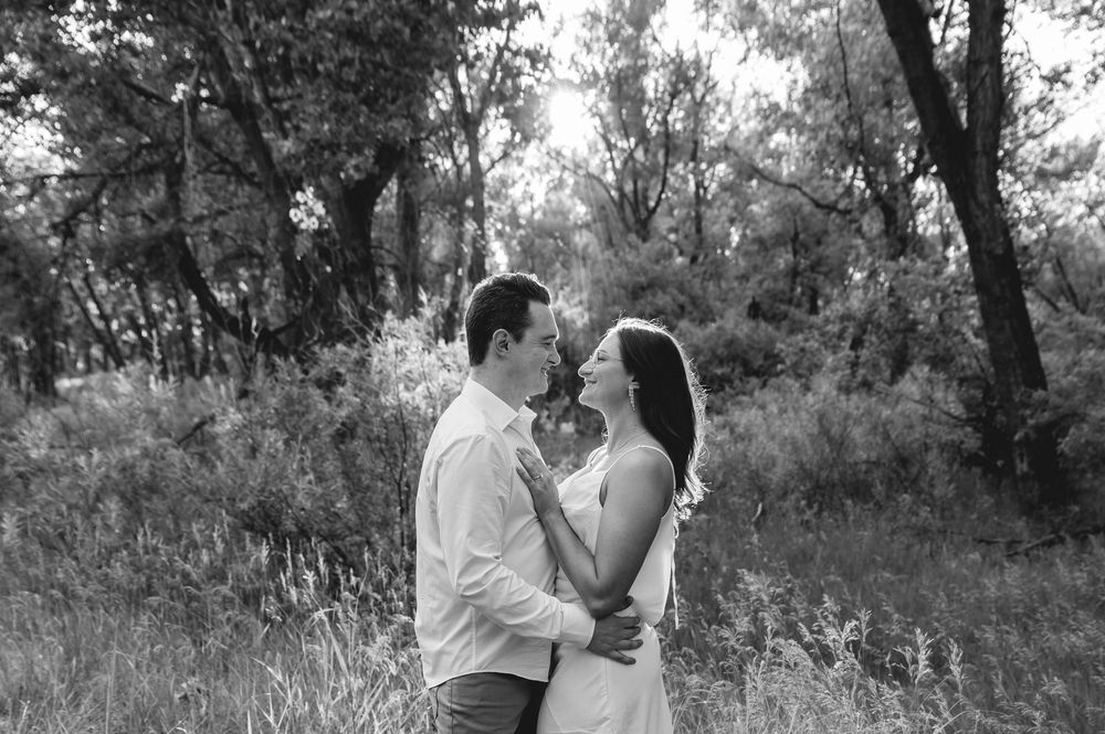 A romantic couple shares a tender moment outside in a wooded area during a black and white photo session.