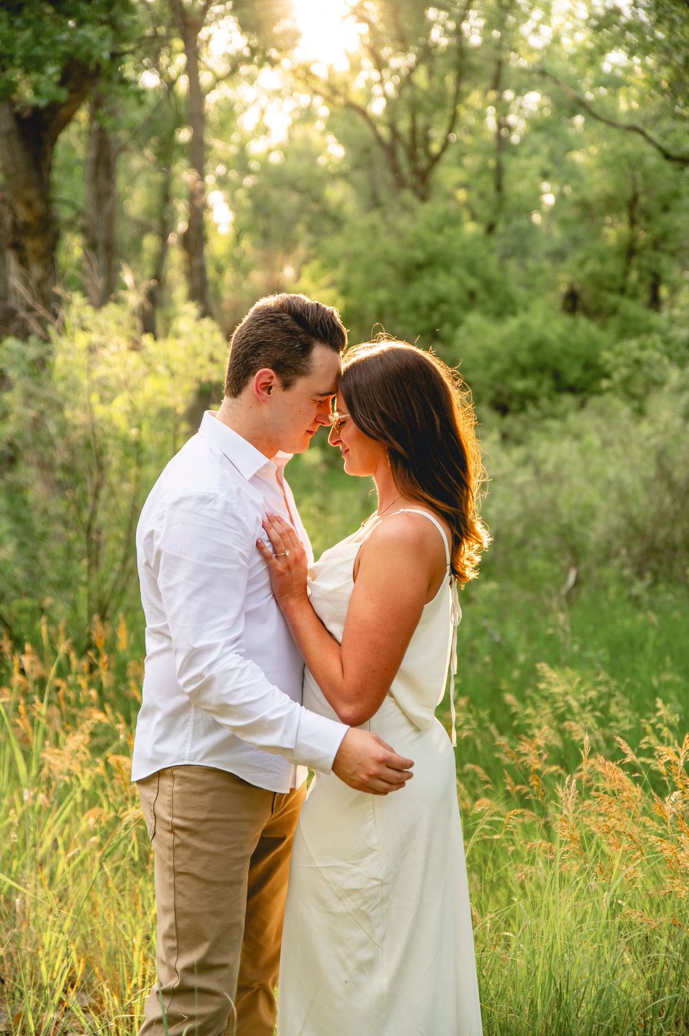 A romantic couple shares an intimate moment in a sunlit meadow during golden hour.