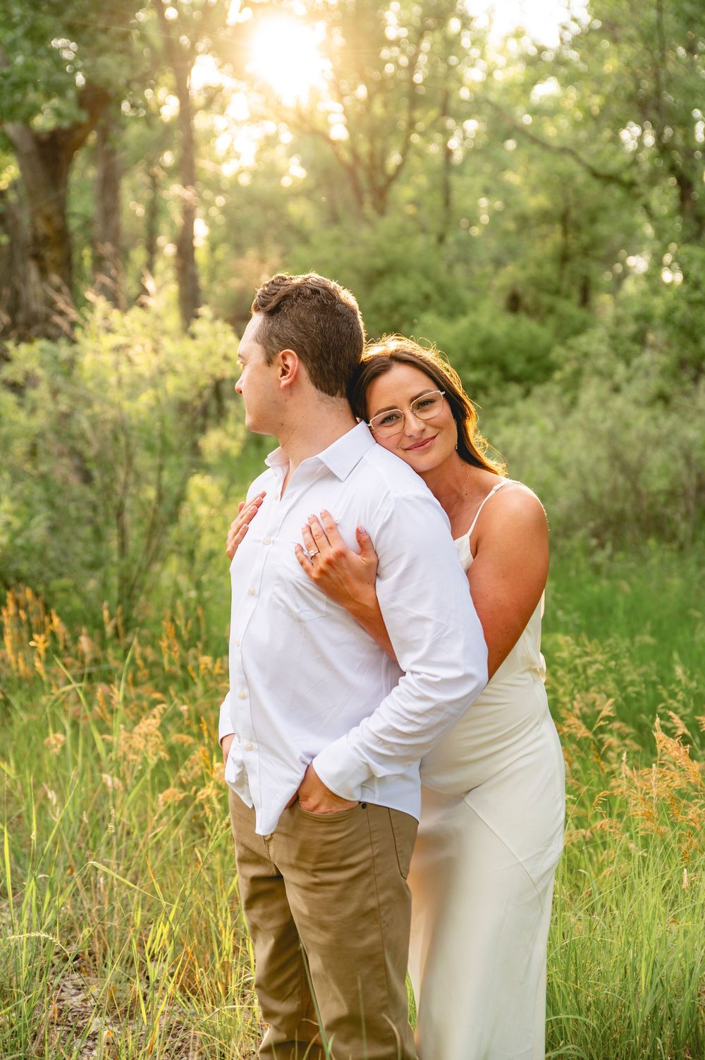 Romantic outdoor couples portrait with warm sunset lighting in a natural forest setting wearing white and khaki outfits.