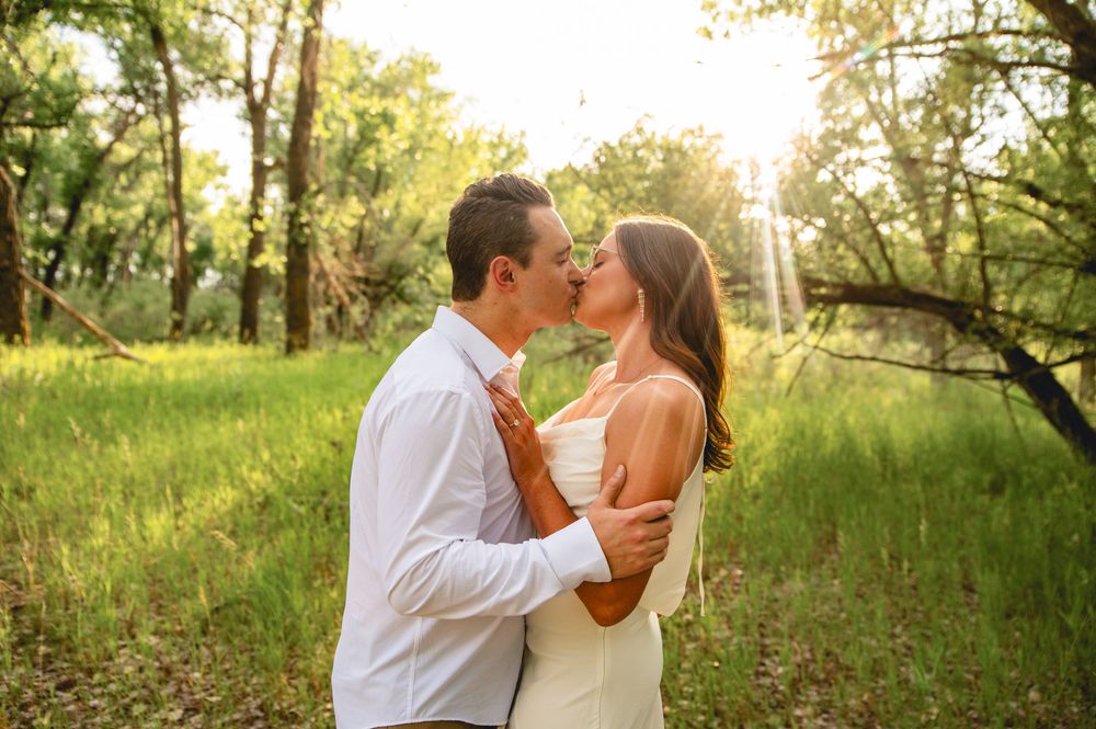 Couple sharing a romantic moment in a sunlit meadow surrounded by trees during golden hour.