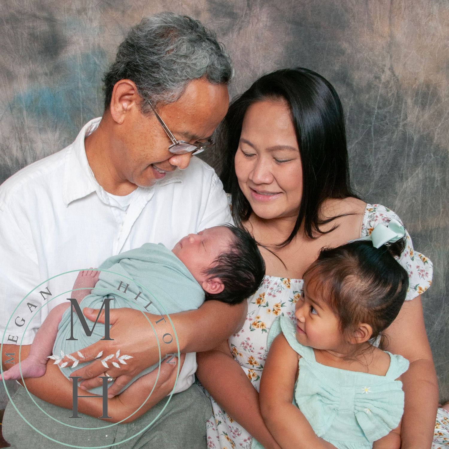 Photo of parents and toddler looking down and a newborn baby.