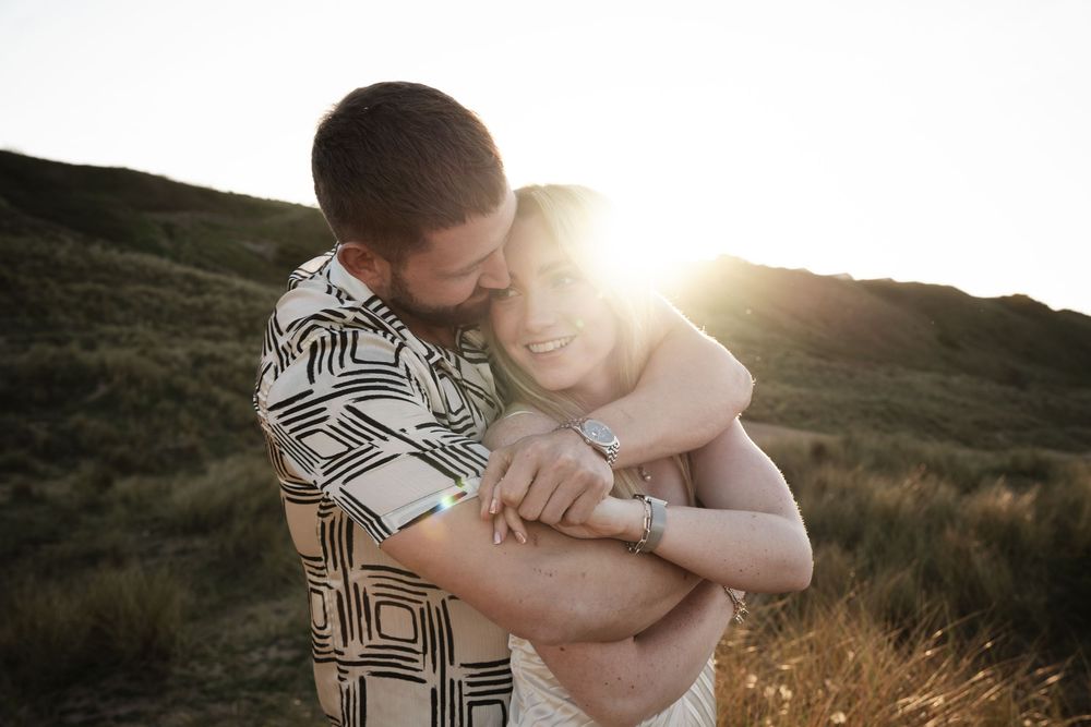 Two people embrace in a tender hug while standing in a field during golden hour sunset.