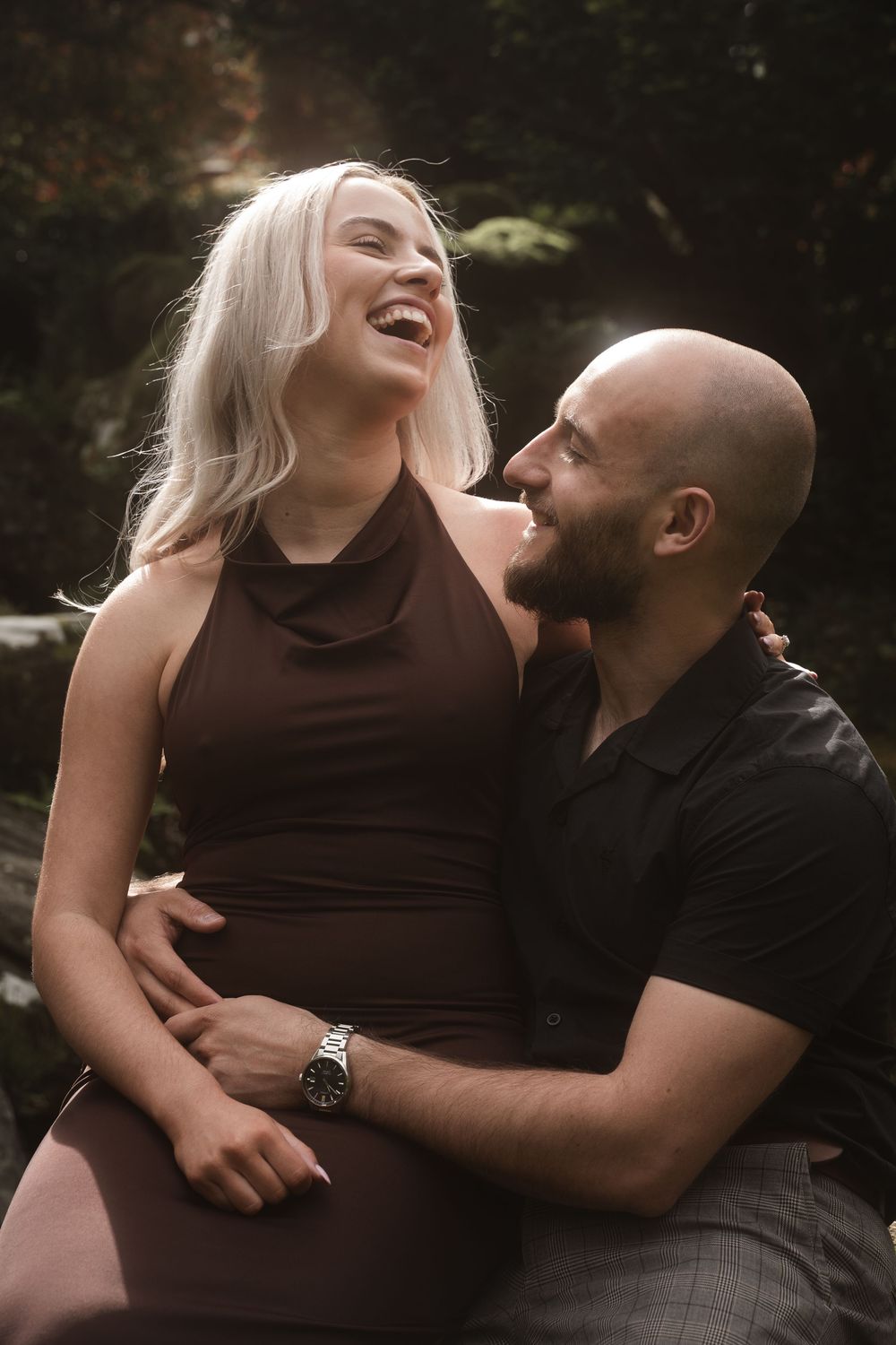 A couple sharing joyful laughter during an intimate outdoor photo session in natural lighting.