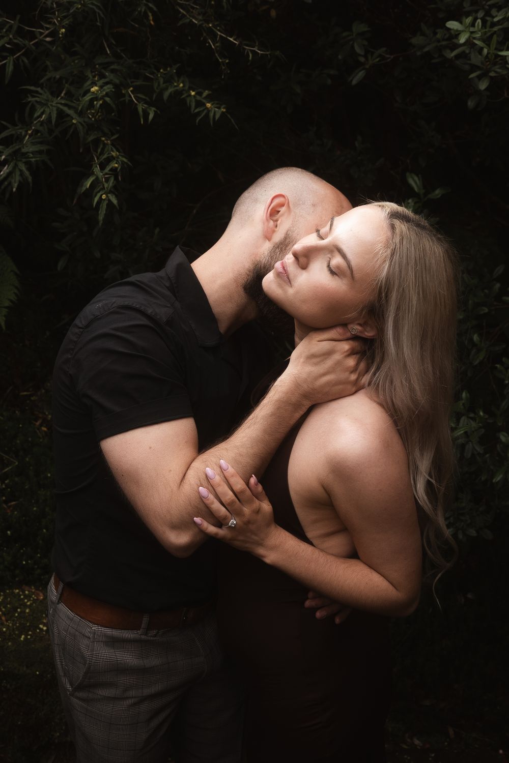 A couple embraces intimately against a dark foliage backdrop in this romantic photo sequence.