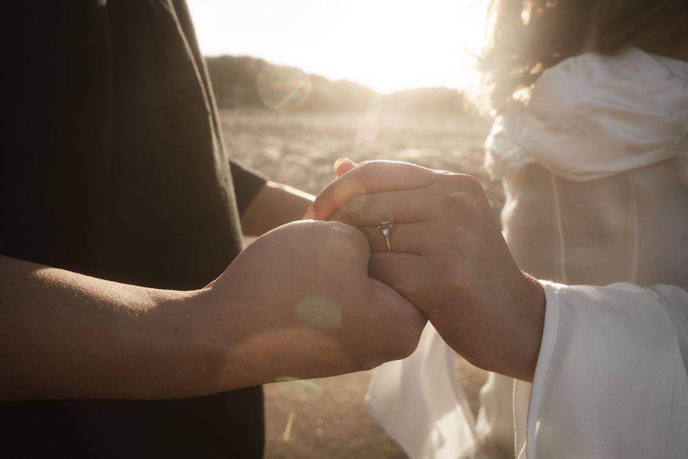 Two hands exchanging wedding rings during a romantic sunset ceremony outdoors.