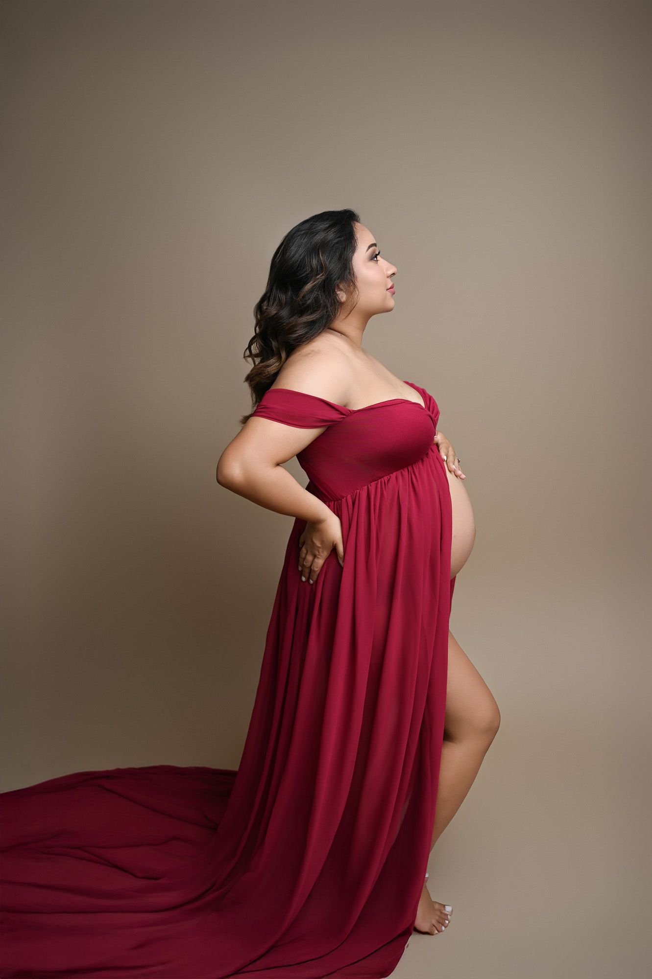 Pregnant woman in red gown posing side-profile during a Central California studio maternity photo session.