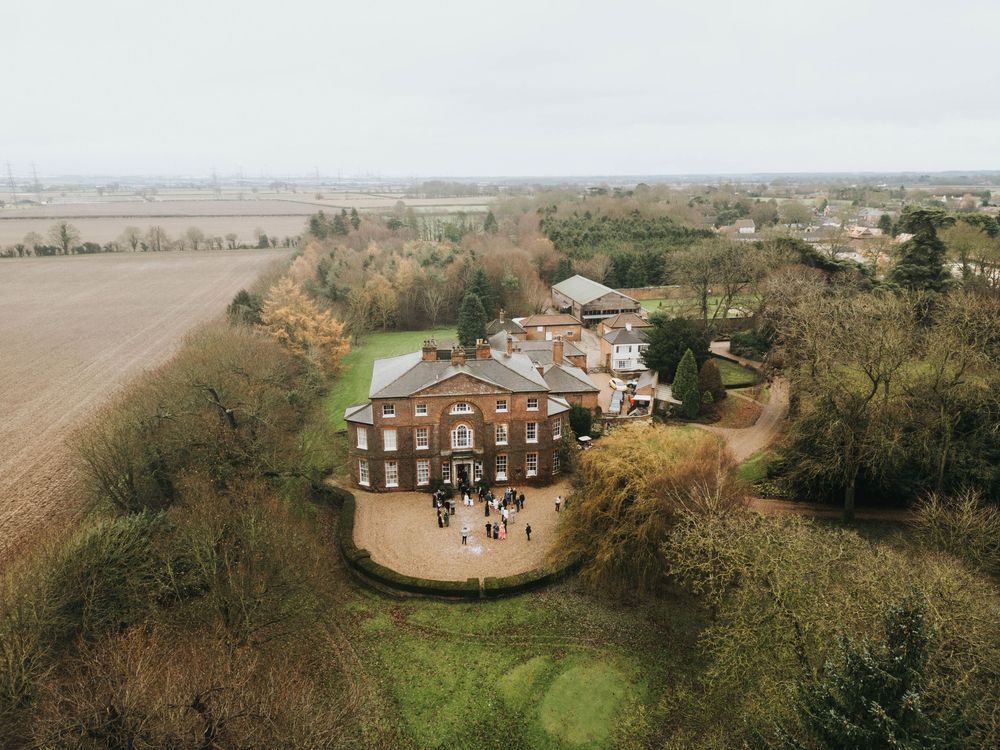 Drone aerial view of a historic brick mansion and its surrounding gardens on a cloudy autumn day.