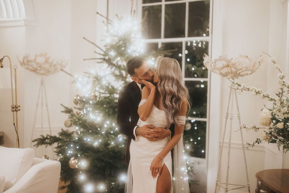 Romantic holiday moment with glowing Christmas tree by window with couple embracing in soft warm light.
