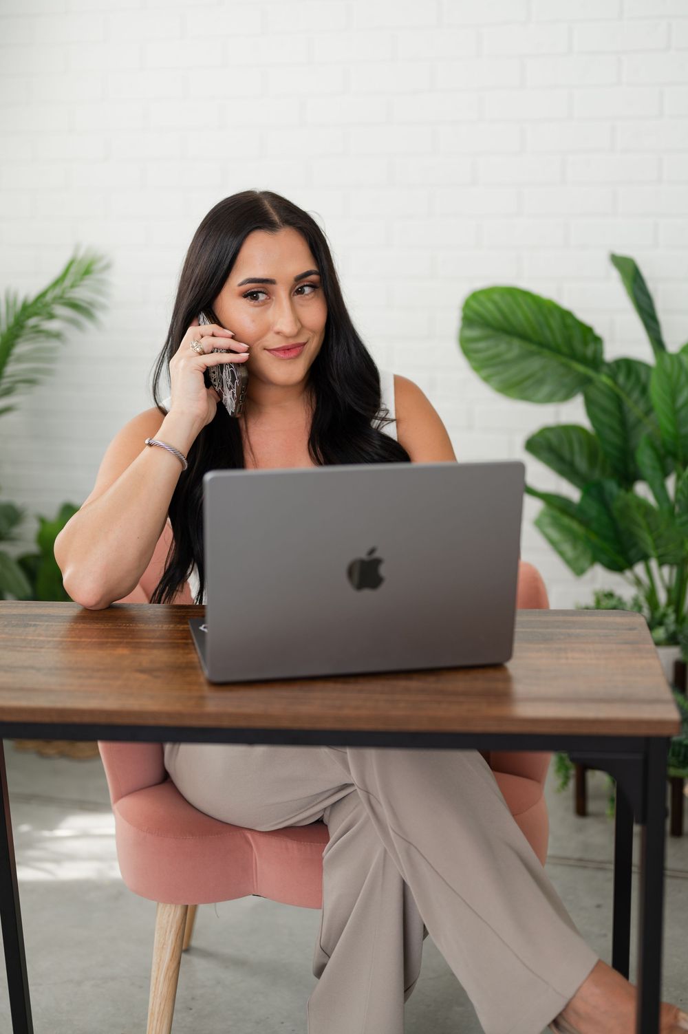 Professional captures someone working remotely at a wooden desk with houseplants and a MacBook laptop in a bright setting.