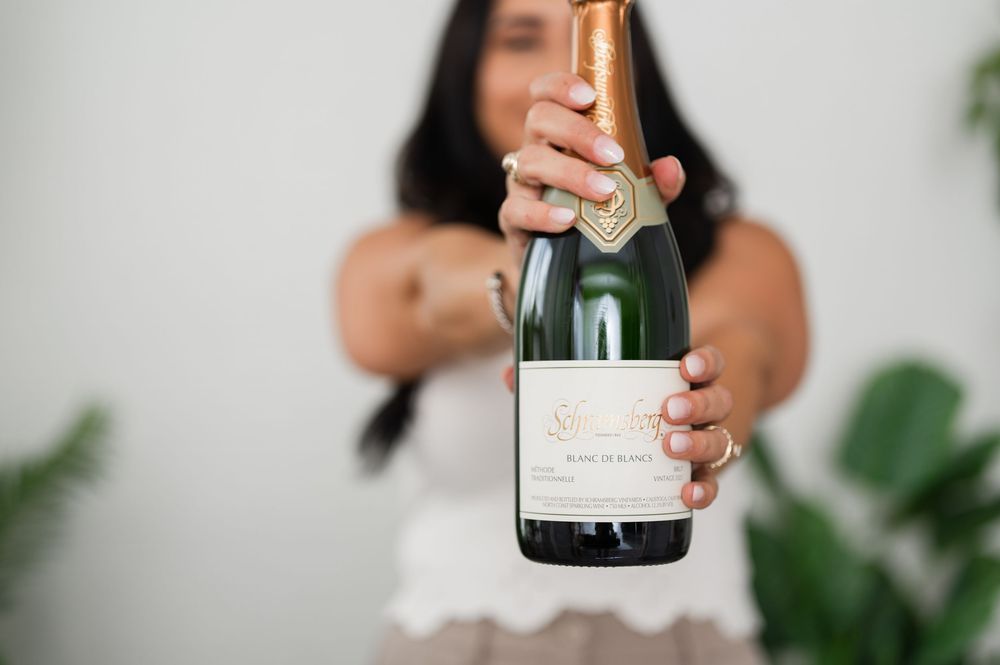A champagne bottle being poured in a minimalist setting with green plants in the background.