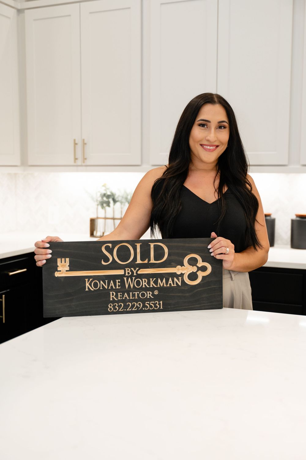 Professional showcasing real estate name plate signage with contact information in modern white kitchen setting.