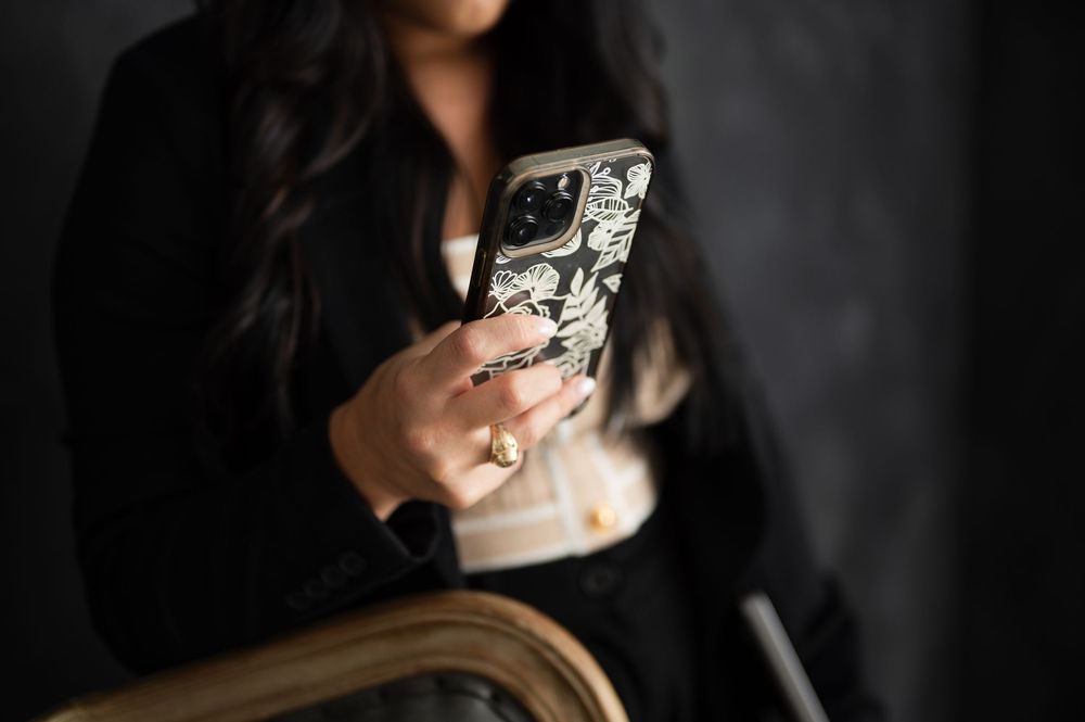 Someone using a phone with decorative case while sitting in vintage wooden chair against dark background.