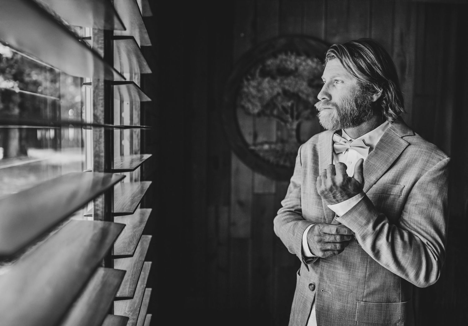 Groom adjusting his tie near a window with soft natural light