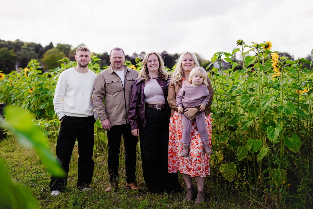 Group standing in front of tall sunflower field on cloudy summer day.