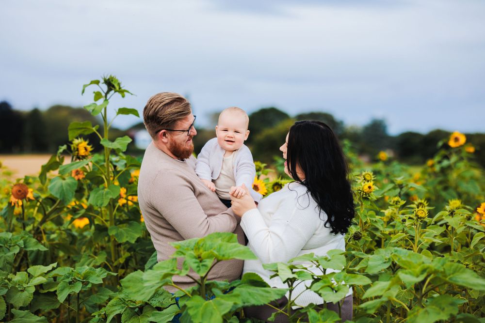 Intimate family moment shared among blooming sunflowers on cloudy day.