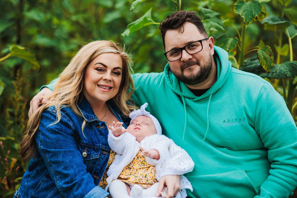 Casual family portrait in a garden setting with greenery and soft natural lighting.