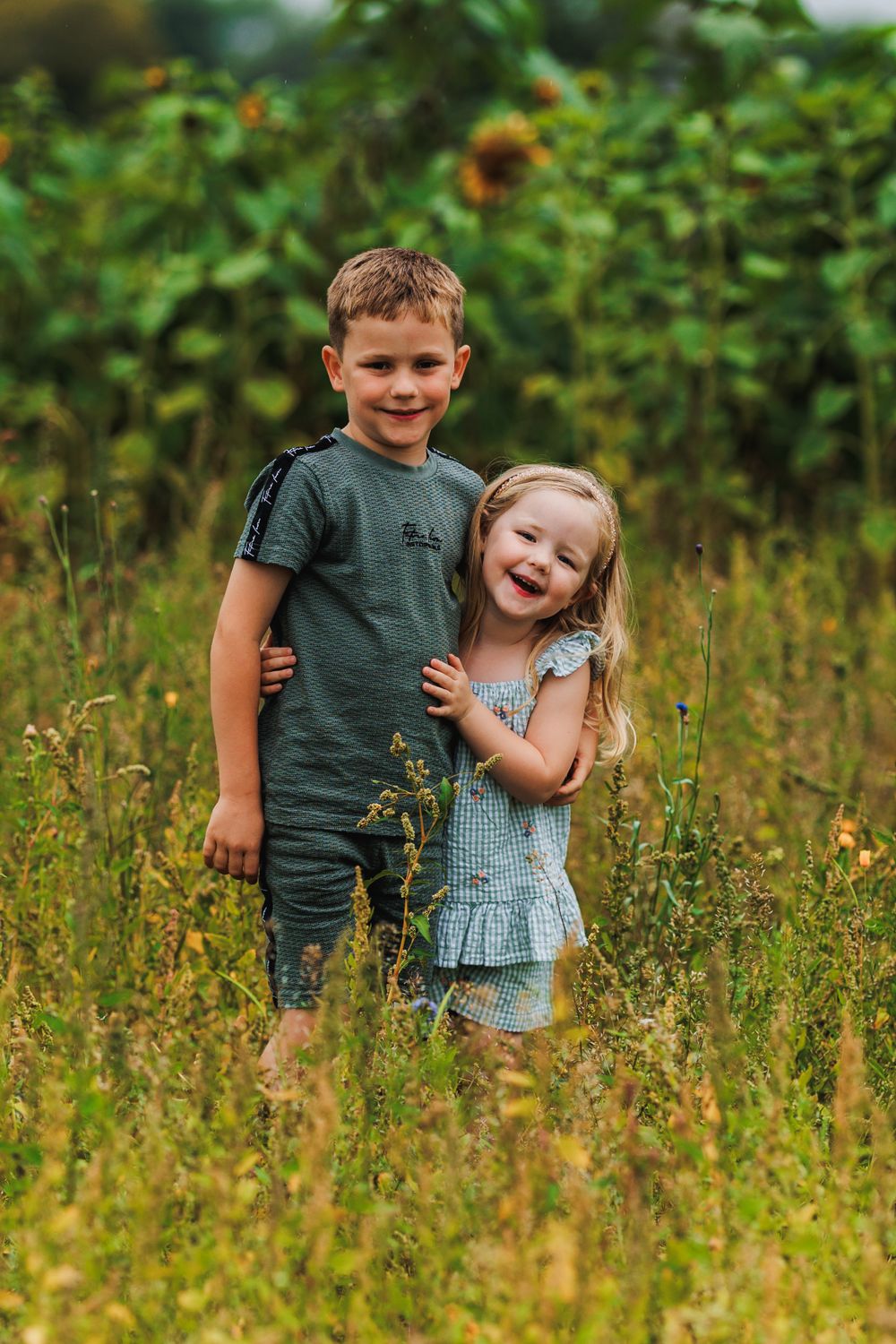 Sweet sibling moment captured in tall grass and wildflowers during golden hour.