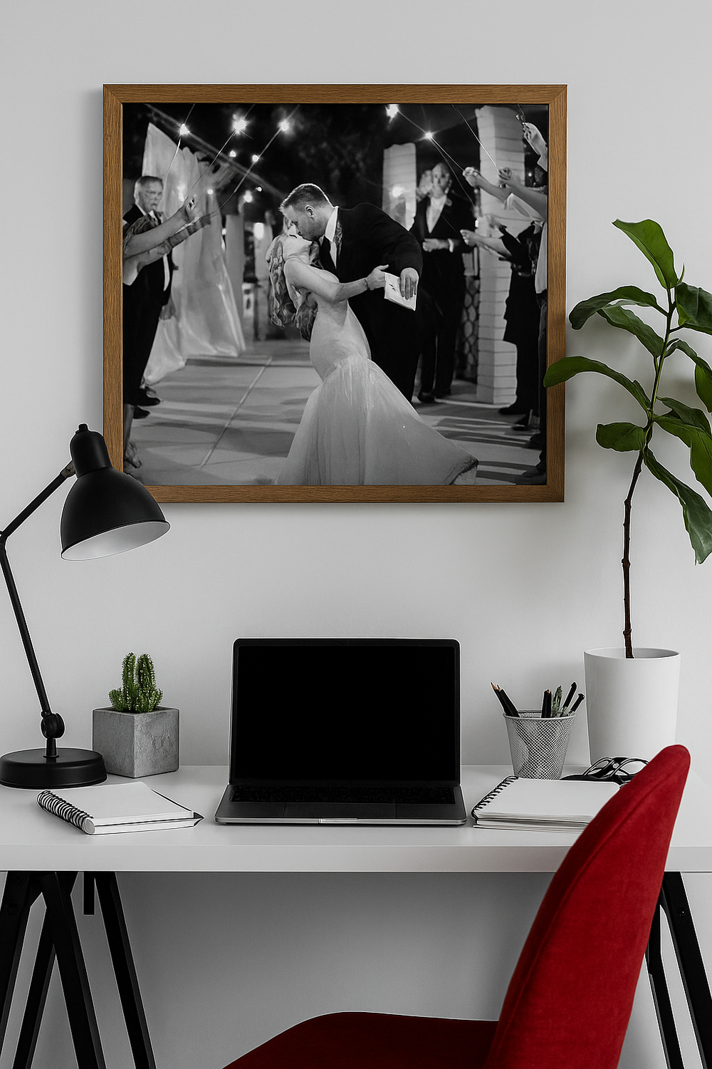 Modern home office workspace with white desk, red chairs, and black and white wedding photographs displayed on wall.