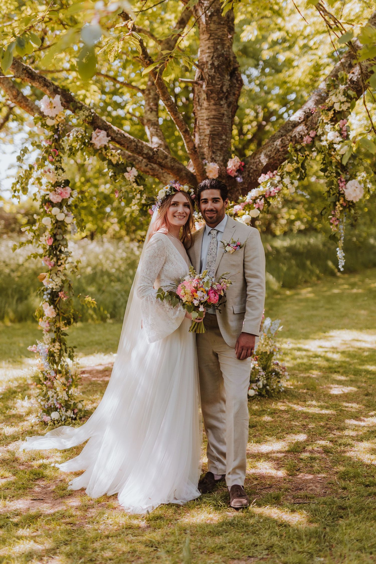A sunny garden wedding ceremony under a blossoming tree with hanging floral details