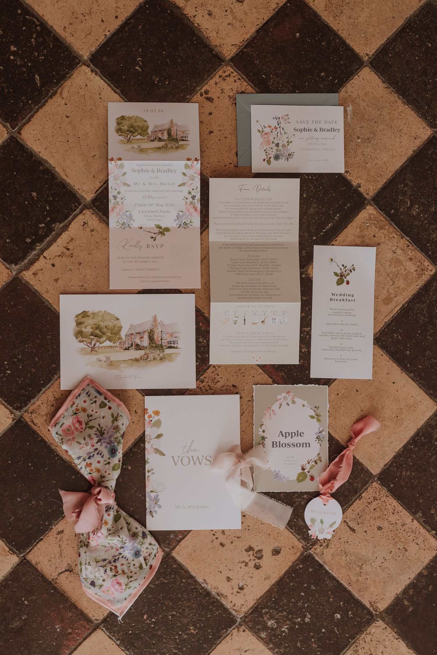 Elegant wedding invitation suite with floral designs and watercolor illustrations laid out on a checkered stone floor.