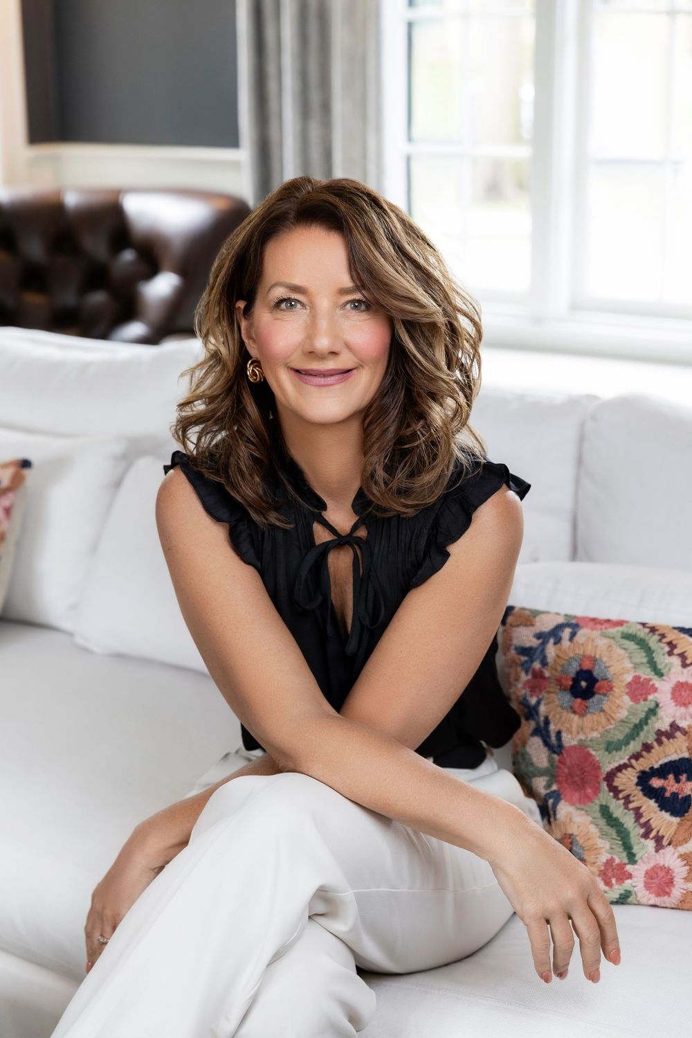 Four lifestyle photos showing a woman in a black top lounging on white furniture with floral pillows in a bright room.