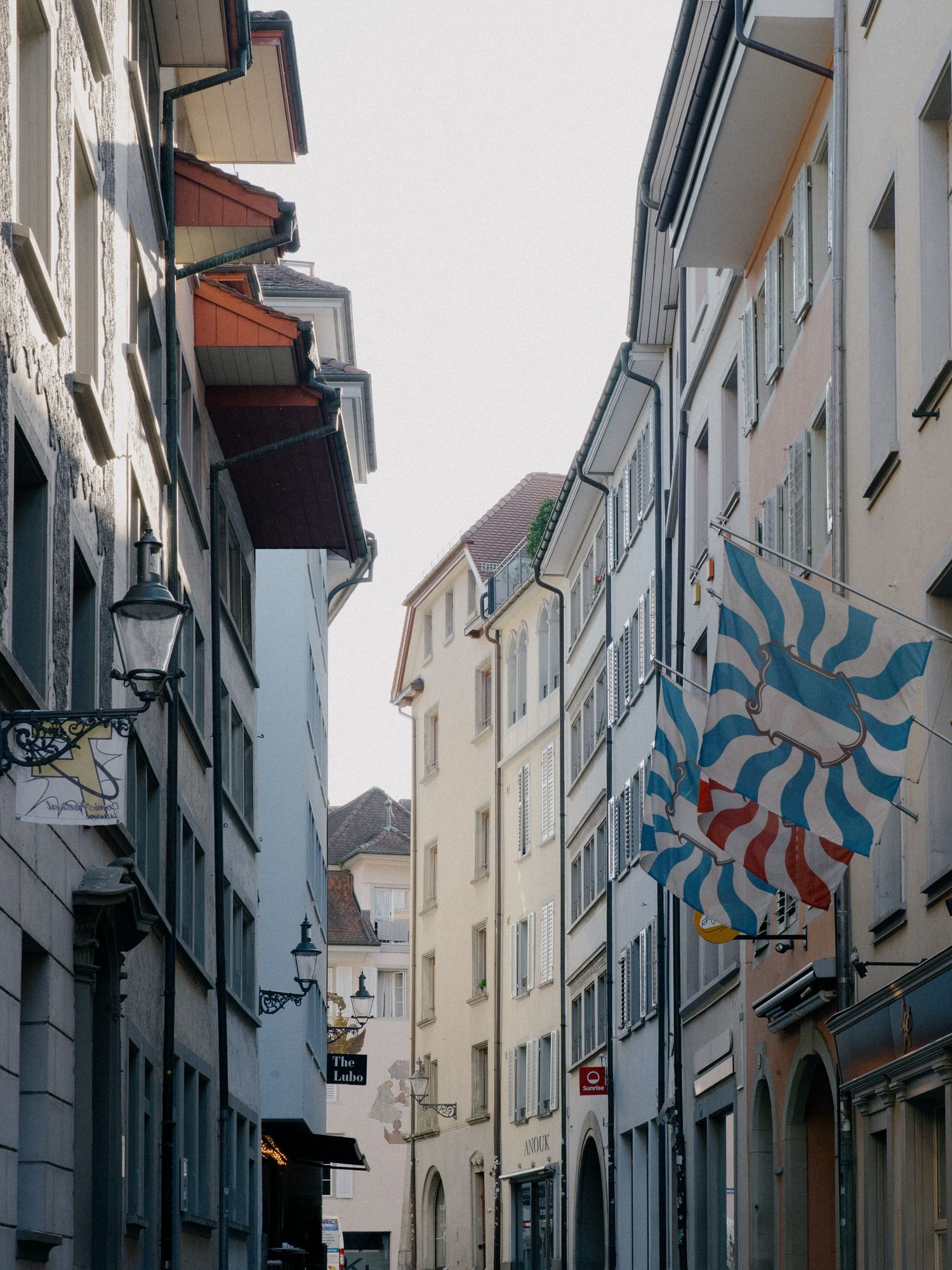 A narrow cobblestone street in a European old town with traditional architecture and a colorful flag on display.