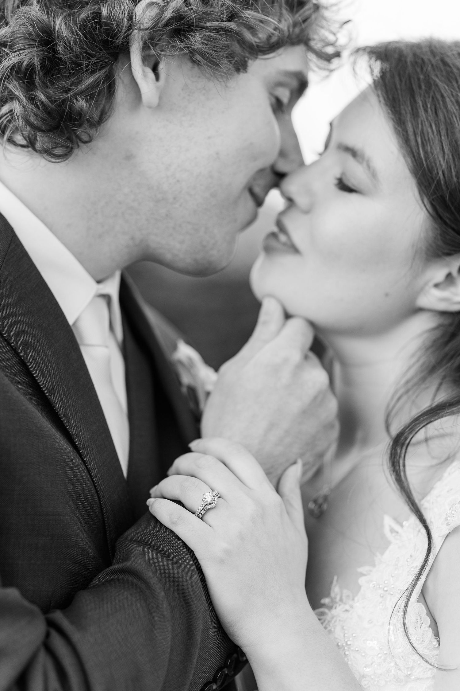 Black and white romantic wedding photograph of a couple sharing an intimate kiss with a diamond ring visible on the bride's hand.
