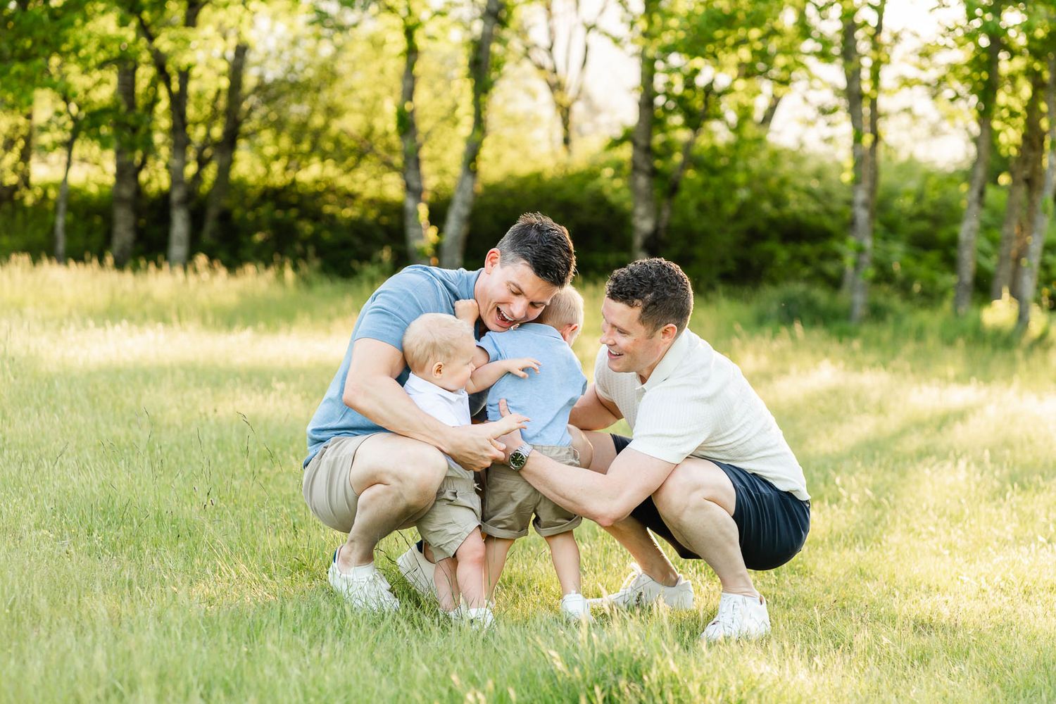 Two dads hug their sons at a park at sunset.