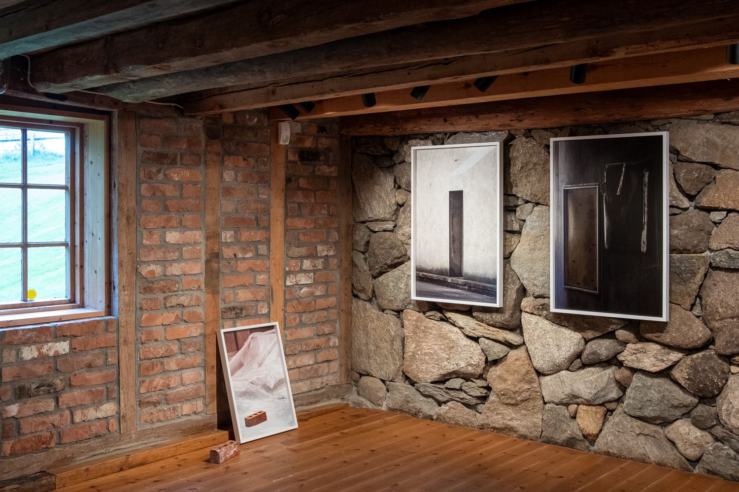 Two framed prints on rock wall and one print leaning on brick wall with a brick beside it, Fotland mølle, Aug–Sept 2024.