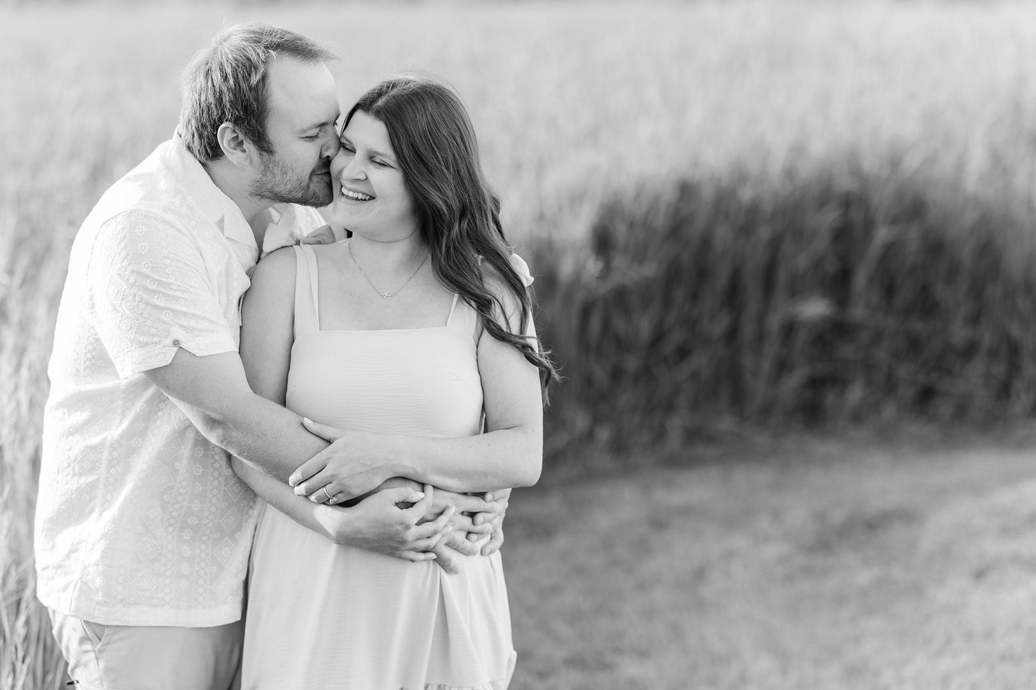 A romantic black and white portrait of an intimate couple embracing in a natural outdoor setting.