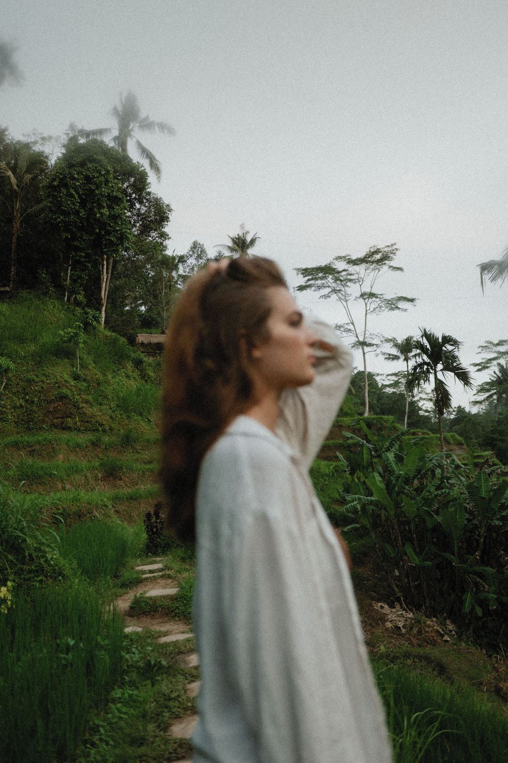 Artistic portrait of person in white shirt on winding path through tropical foliage.