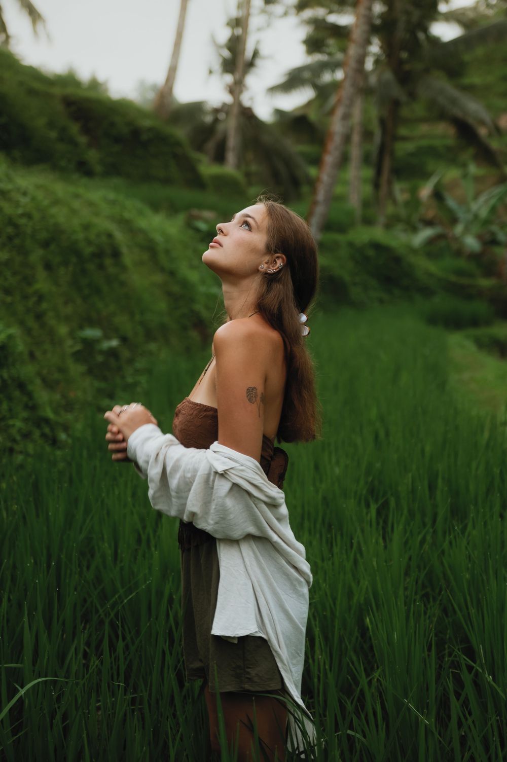 Someone wearing a white top poses expressively against a backdrop of verdant rice fields and palm trees.