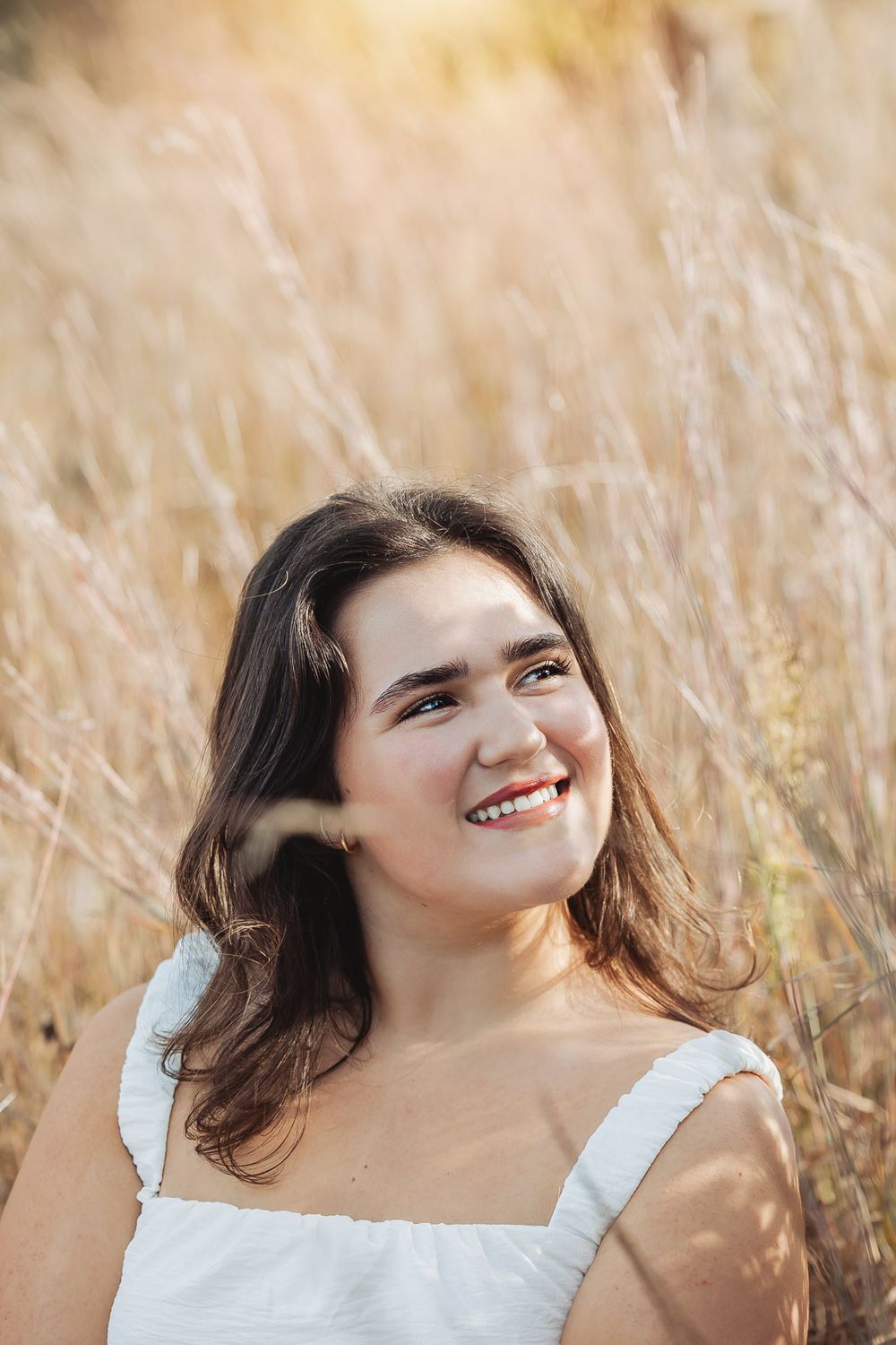 Person relaxing in golden wheat field on sunny day wearing white top and smiling at sunset.
