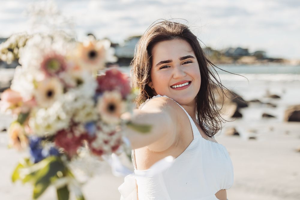 A joyful seaside portrait captured in natural light with the beach and ocean waves in the background.
