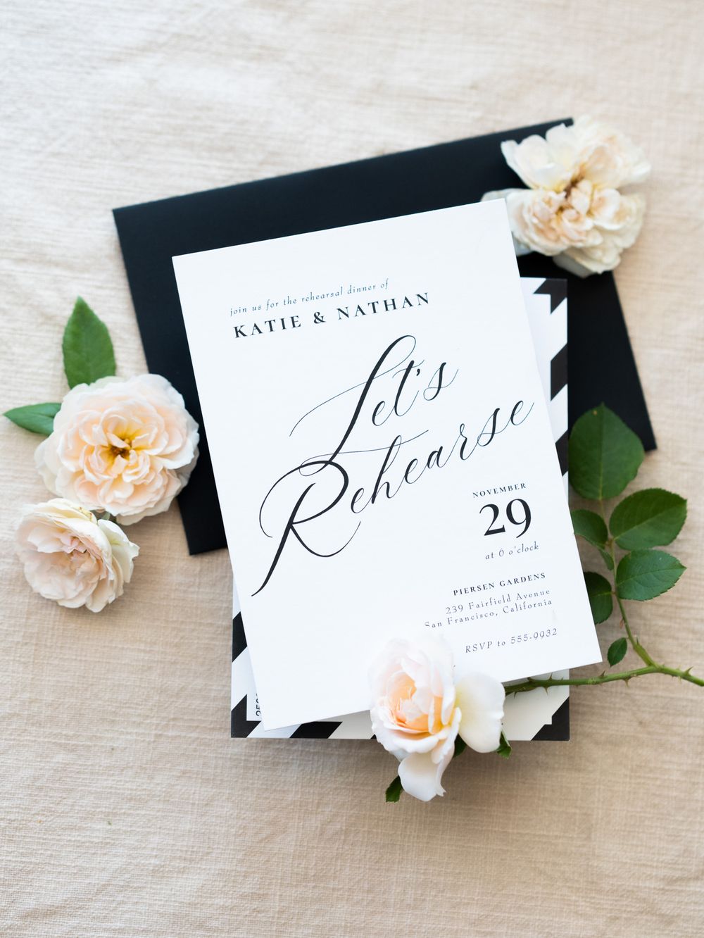 White calligraphy wedding place cards displayed with delicate peach roses and green leaves on a light gray surface.