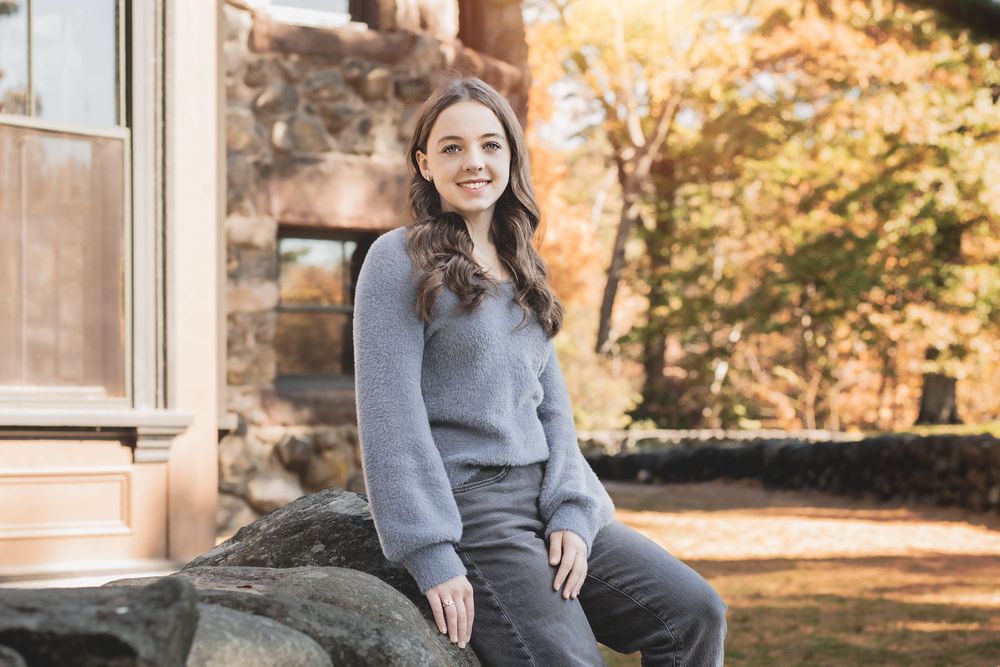 Autumn outdoor photography session with subject sitting on stone steps surrounded by fall foliage.