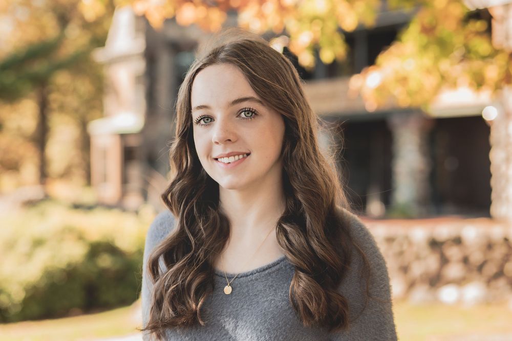 Young model with long brown hair poses outdoors in autumn with warm golden sunlight in the background.