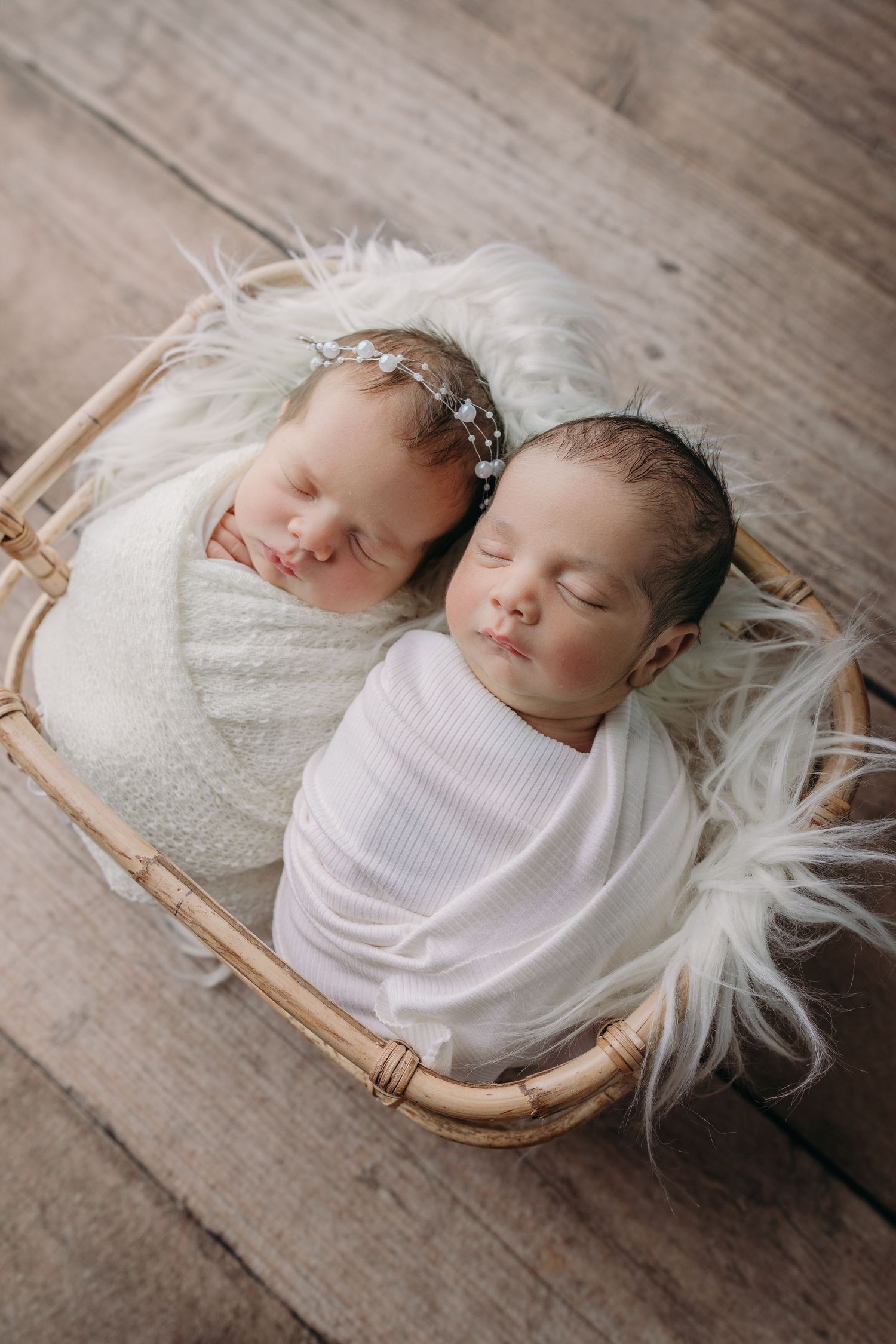 twin newborn photo in basket sleeping peacefully on a rattan basket with fluffy white fur.