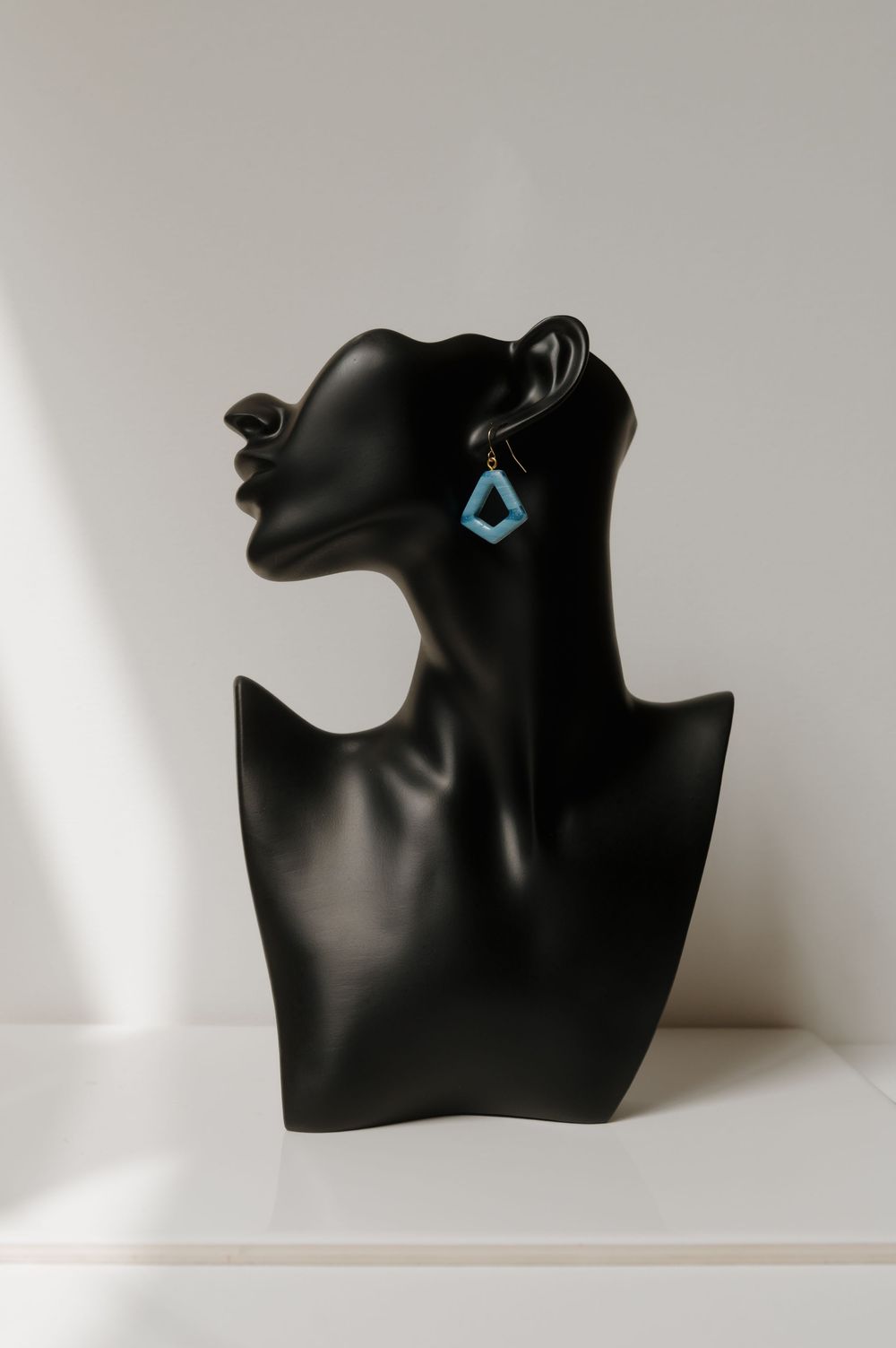 Black jewelry bust mannequin display with turquoise geometric earring against white background.