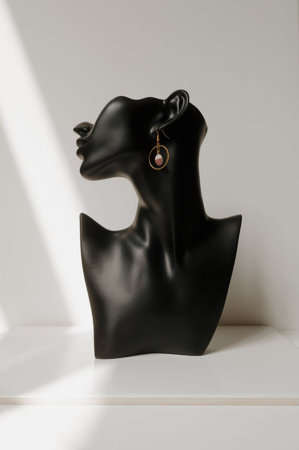 Black jewelry display bust showing an elegant dangle earring against a white background.