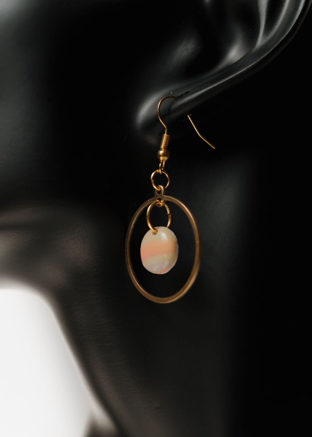 Gold hoop earring with delicate pink moonstone bead pendant photographed against dark background with soft lighting.