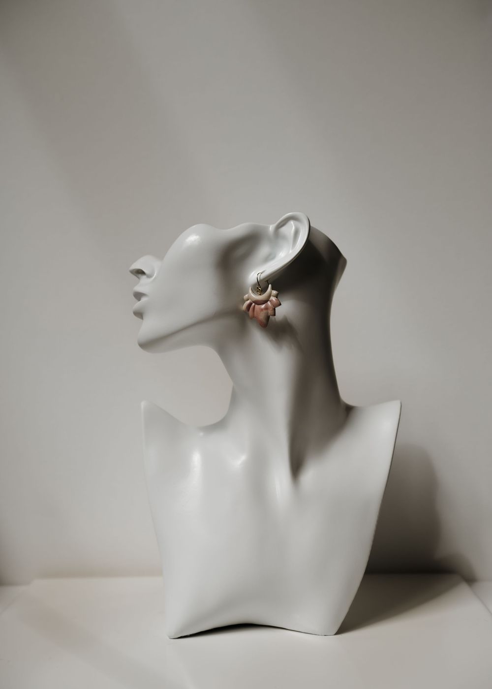 White glossy mannequin jewelry display bust wearing decorative earrings in profile view.