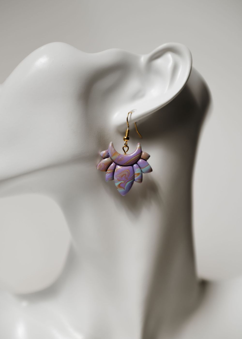 Purple polymer clay lotus flower earring displayed on white mannequin ear against blurred background.