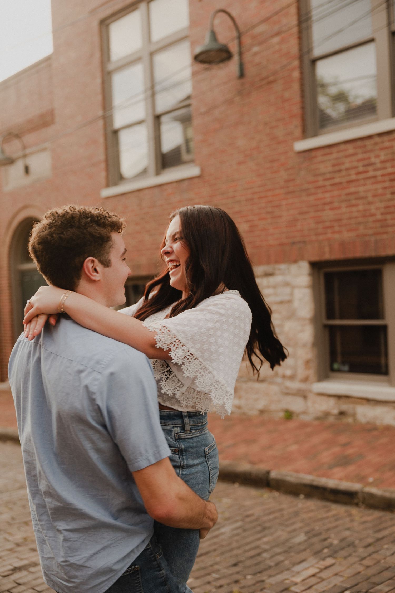 Couple sharing joyful embrace against brick building backdrop.