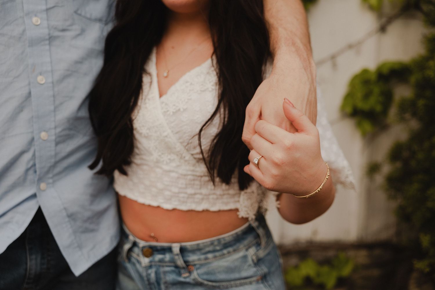 Close-up shot of a couple holding hands wearing casual clothing against a light background.