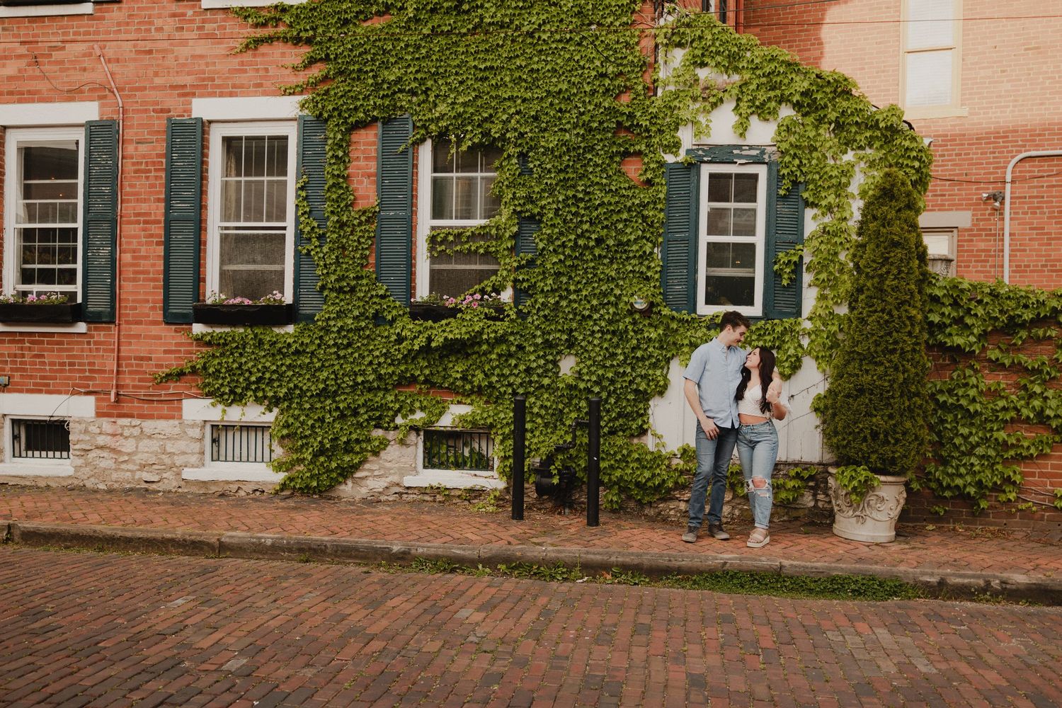 A couple standing by an ivy-covered brick building on a cobblestone street.
