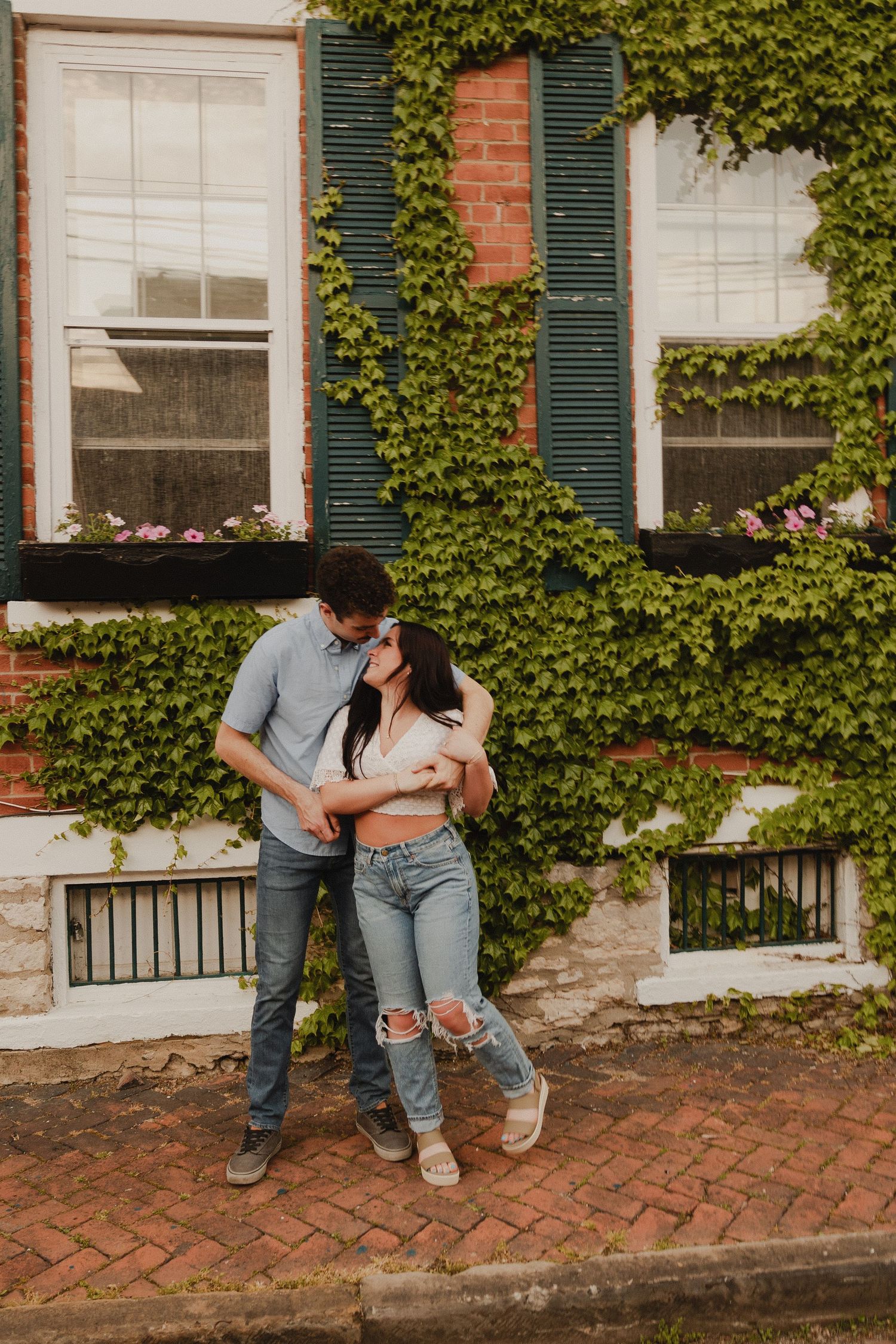 Couple sharing a tender moment against brick and ivy backdrop on historic street.