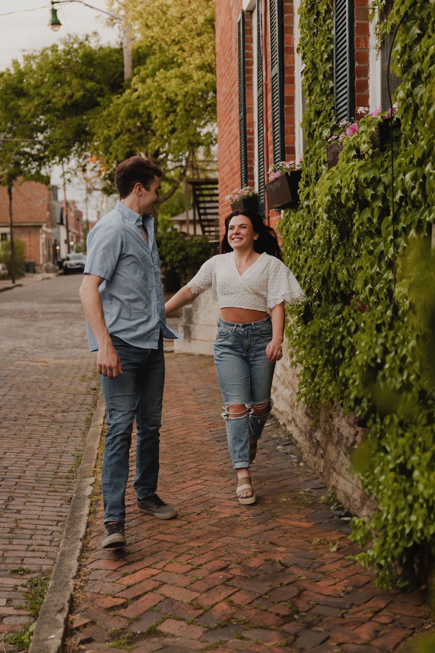 Casual couple walking together on brick sidewalk beside ivy-covered walls.